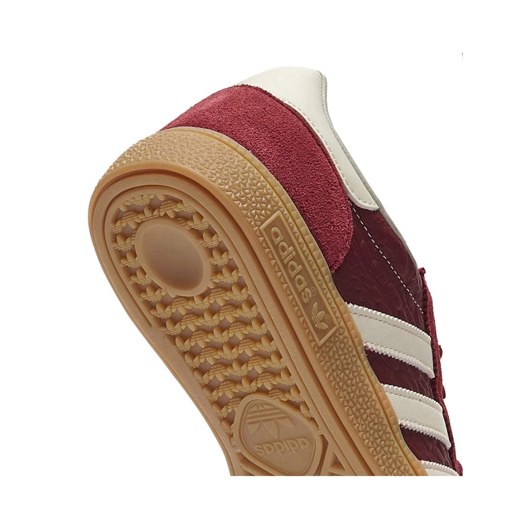 Maroon sneaker with white stripes on a beige sole against a white background