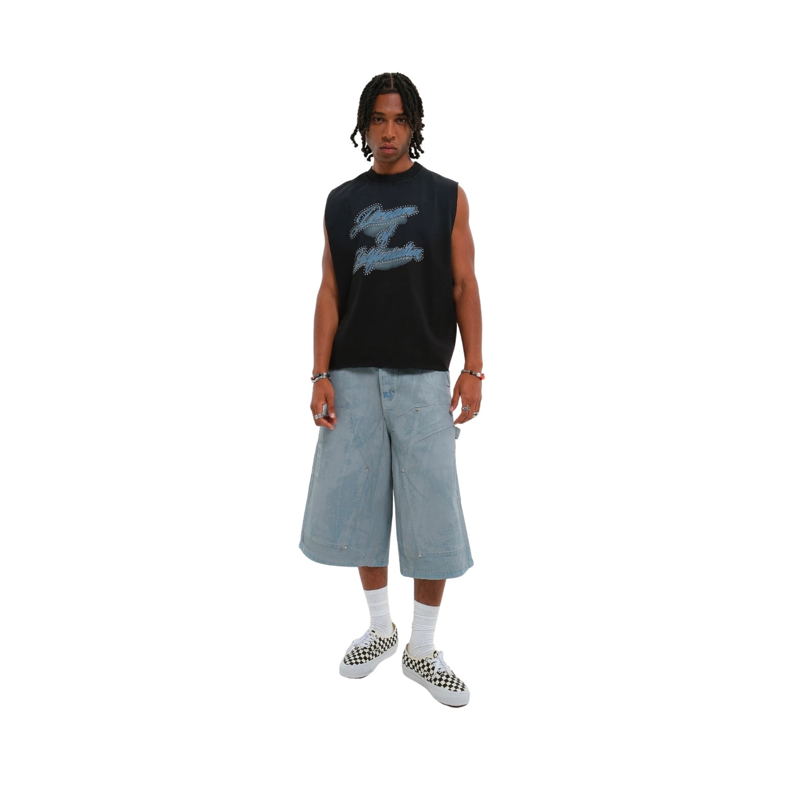 A model stands against a solid white background wearing a black sleeveless tank top with a distressed blue graphic, light-wash denim cropped shorts, white socks, and black-and-white checkered sneakers.