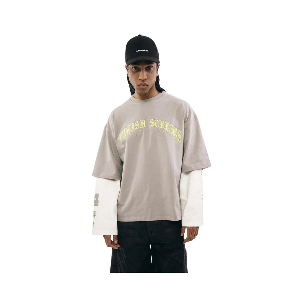 Person wearing a beige long-sleeve shirt with yellow text, white sleeves, and a black cap on a white background