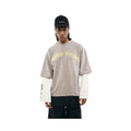 Person wearing a beige long-sleeve shirt with yellow text, white sleeves, and a black cap on a white background