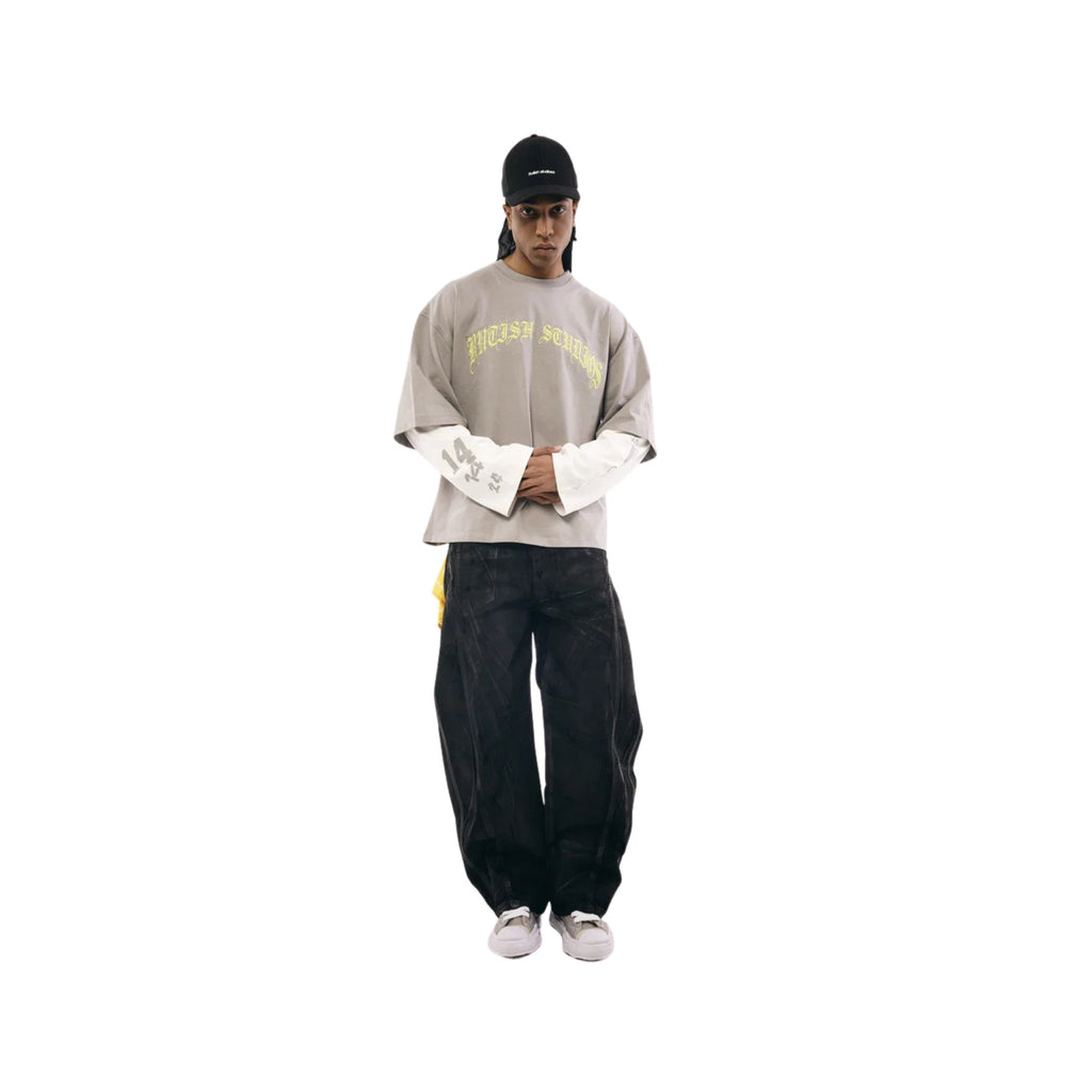 Person wearing a gray sweatshirt with text, black pants, and a black cap on a white background