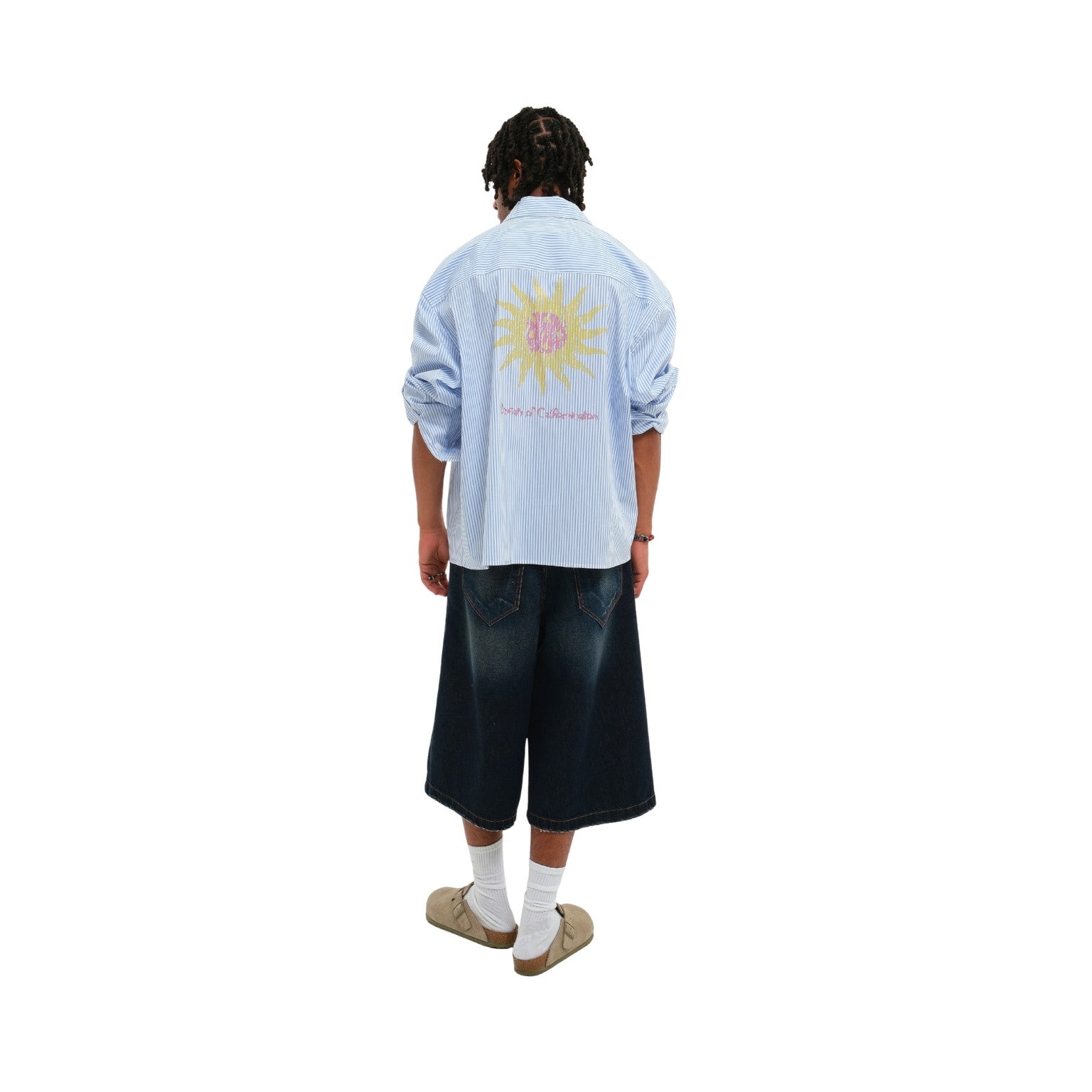 A model shown from the back wearing a light blue striped button-up shirt with a large yellow sun graphic and pink text on the back, paired with dark denim shorts, white socks, and beige shoes, against a plain white background.