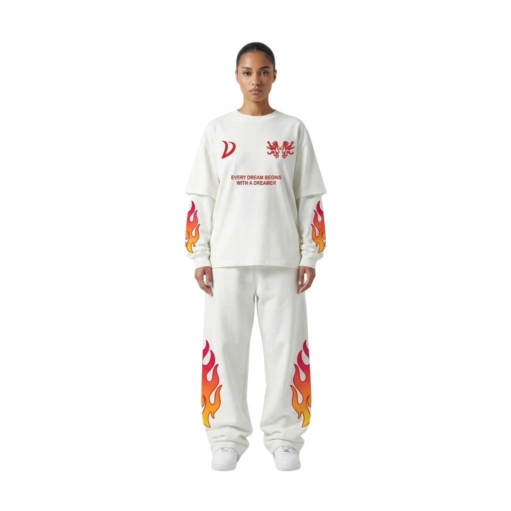 A model stands against a plain white background wearing a matching white sweatshirt and sweatpants set. The sweatshirt features red graphic prints on the chest and sleeve cuffs, while the sweatpants have matching flame graphics on the lower legs.
