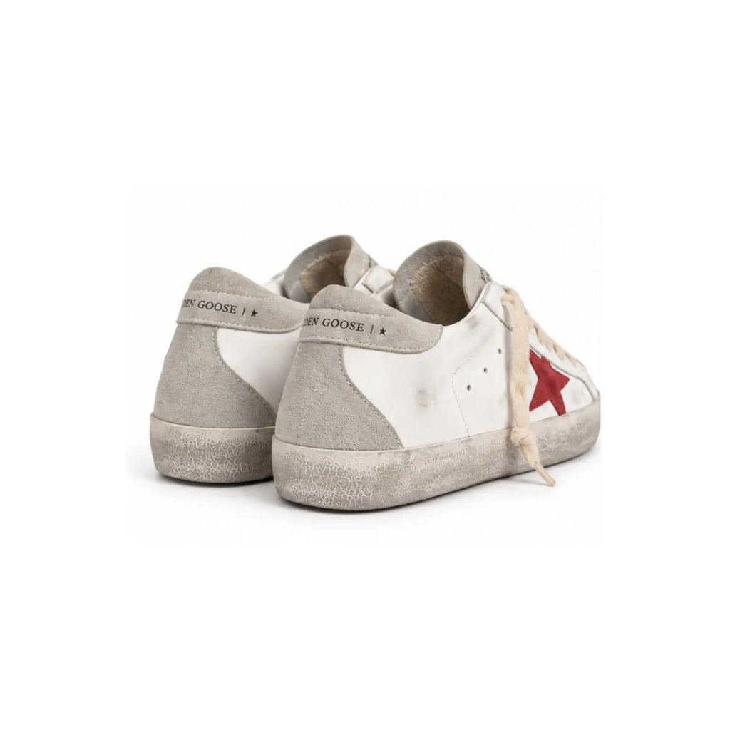 A pair of Golden Goose sneakers in a distressed off-white and light gray suede finish, featuring a signature red star on the side and light beige laces, set against a plain white background.