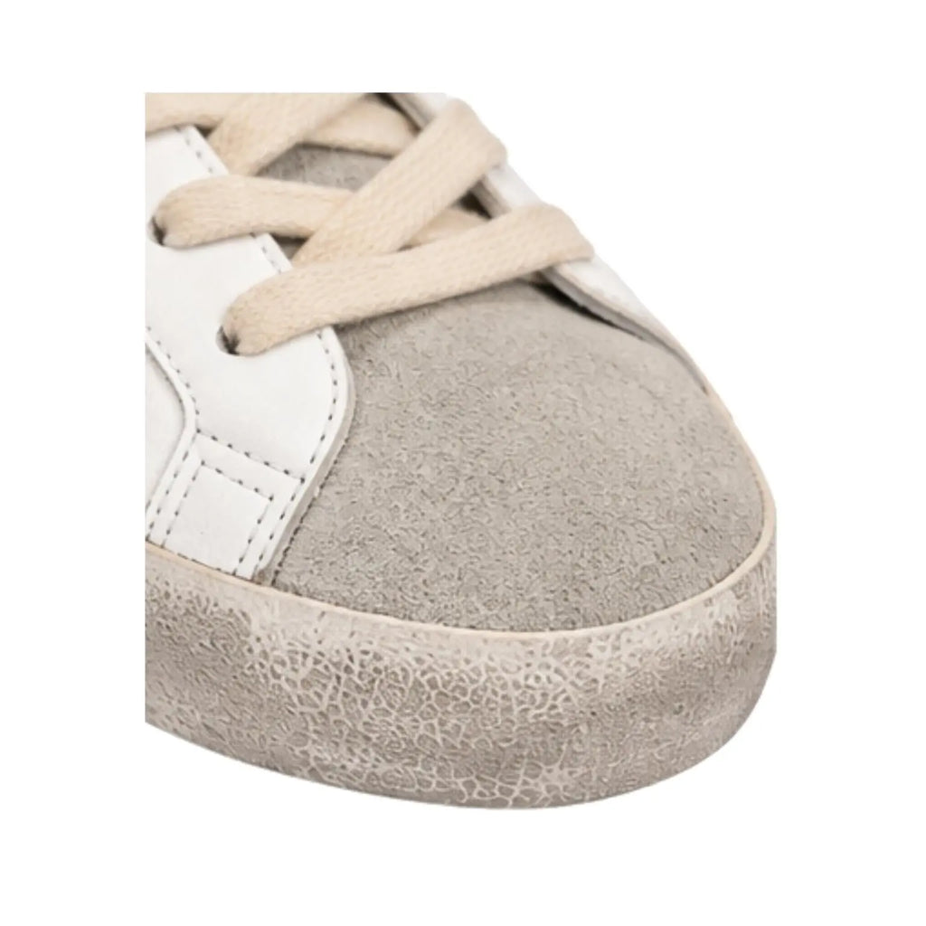 Close-up of a sneaker showing the toe area, featuring a light gray suede toe cap, off-white leather side panels, beige laces, and a distressed off-white rubber sole.