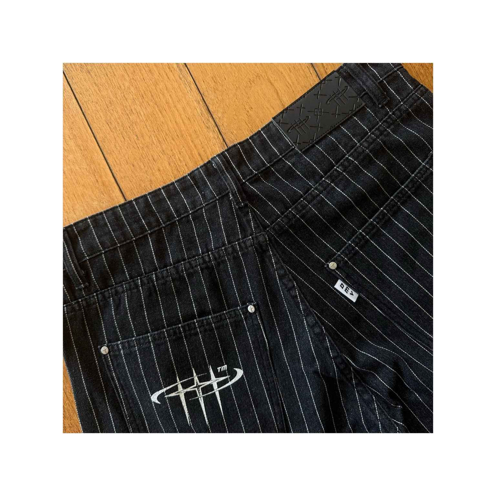 Black pinstripe pants with a logo on a wooden floor