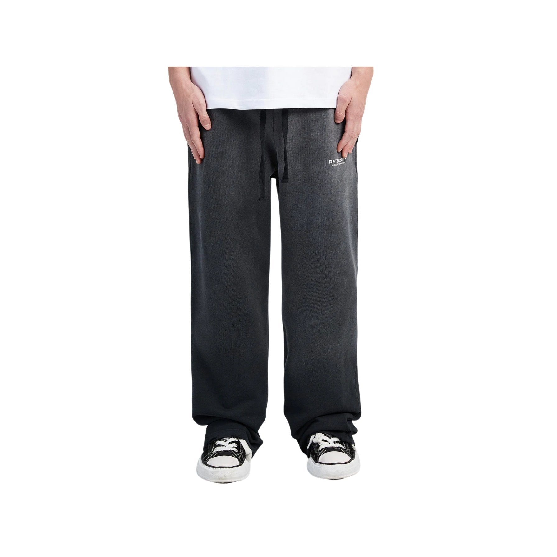 Person wearing black pants and black and white sneakers on a white background
