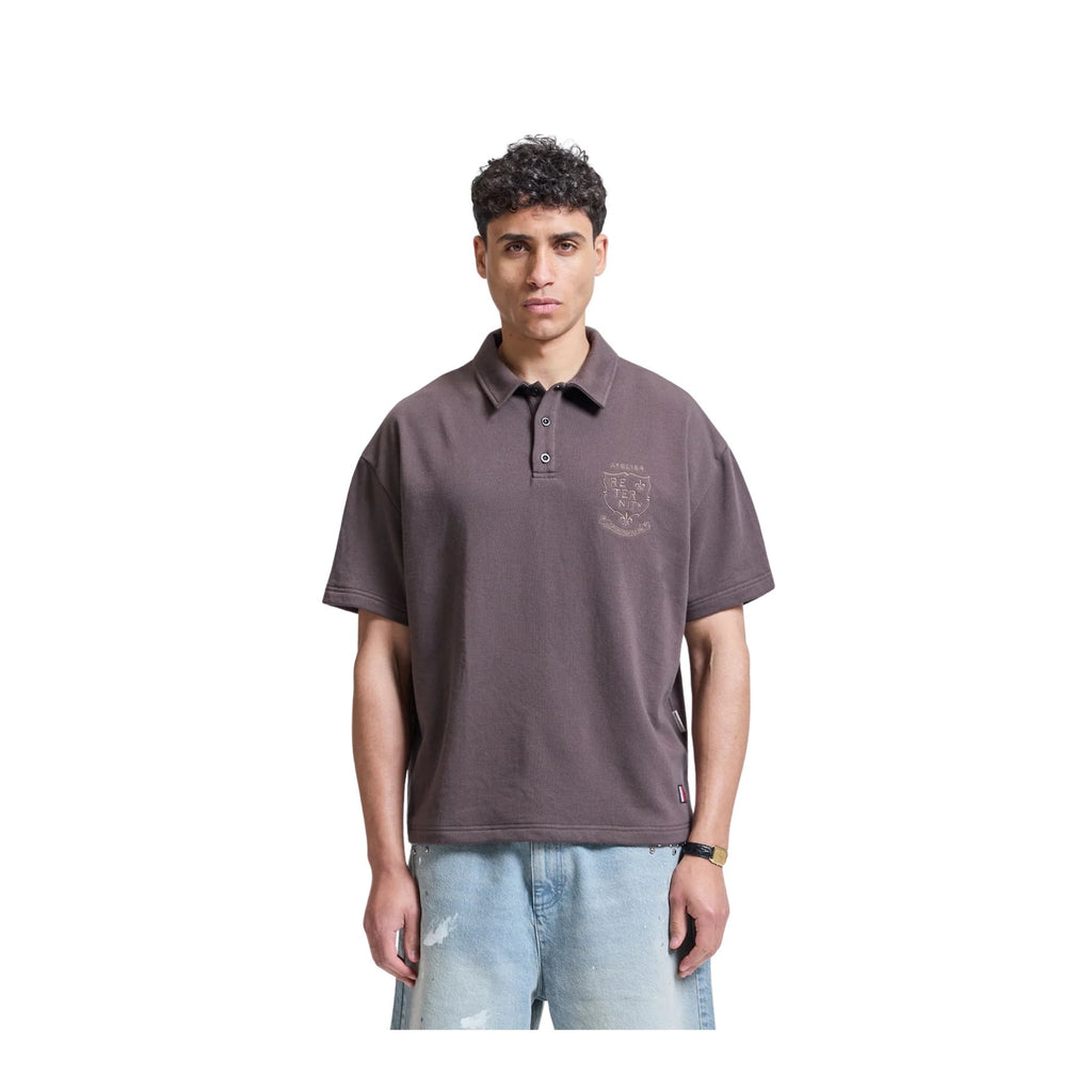 Man wearing a brown polo shirt with a logo on a white background