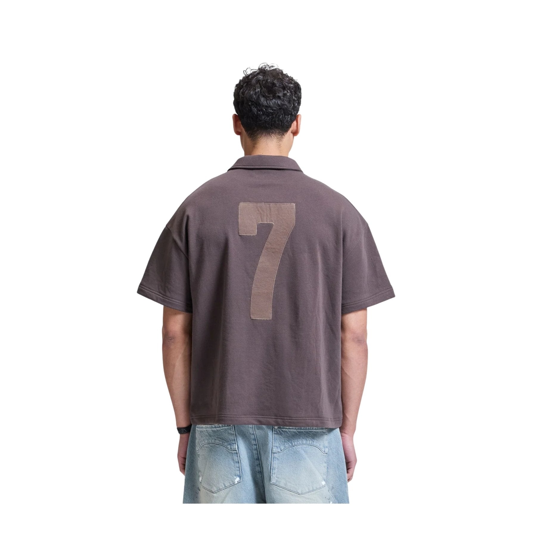 Person wearing a brown polo shirt with the number 7 on the back, standing against a white background
