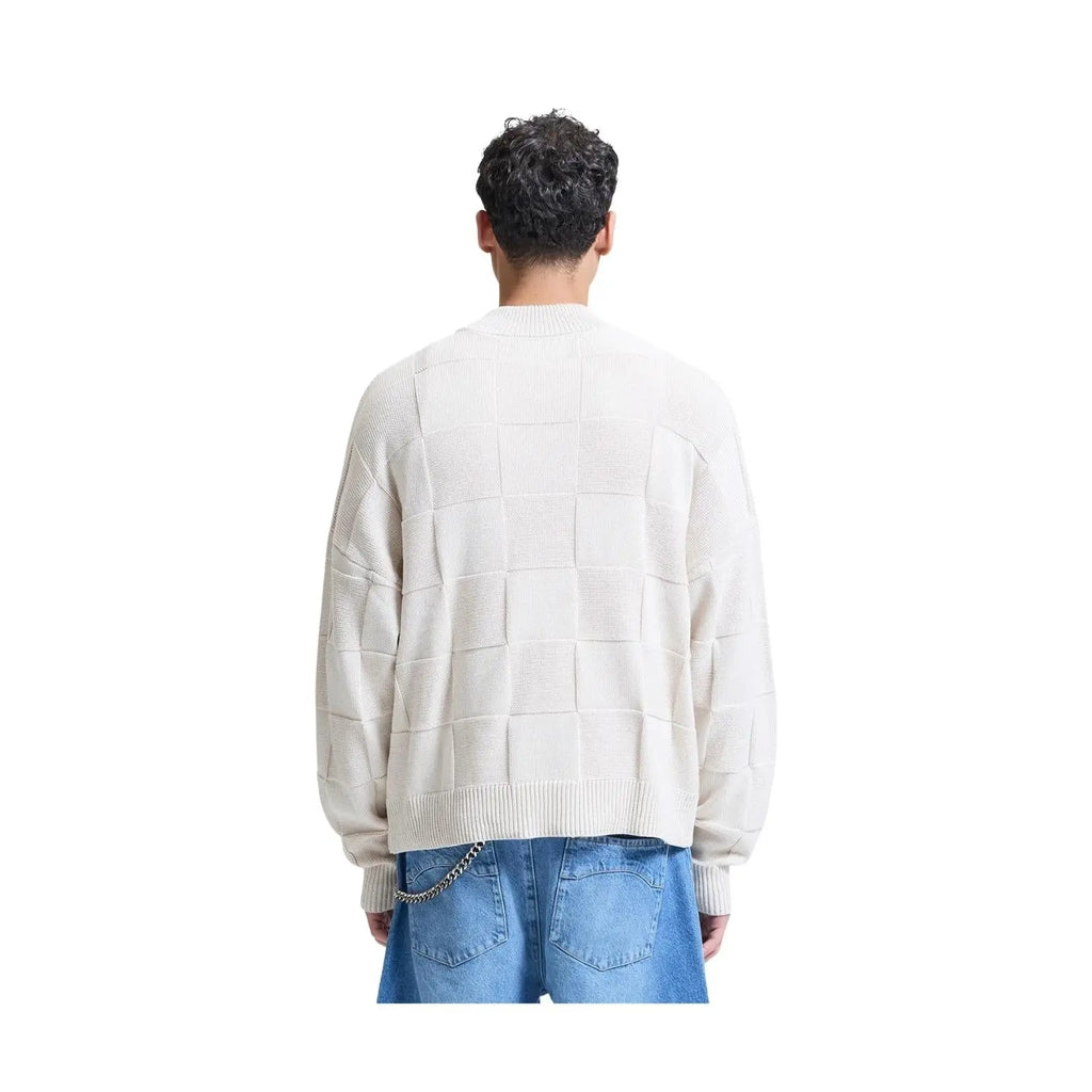 A man viewed from the back wearing a cream-colored knit sweater with a large checkerboard pattern and blue jeans, isolated on a white background.