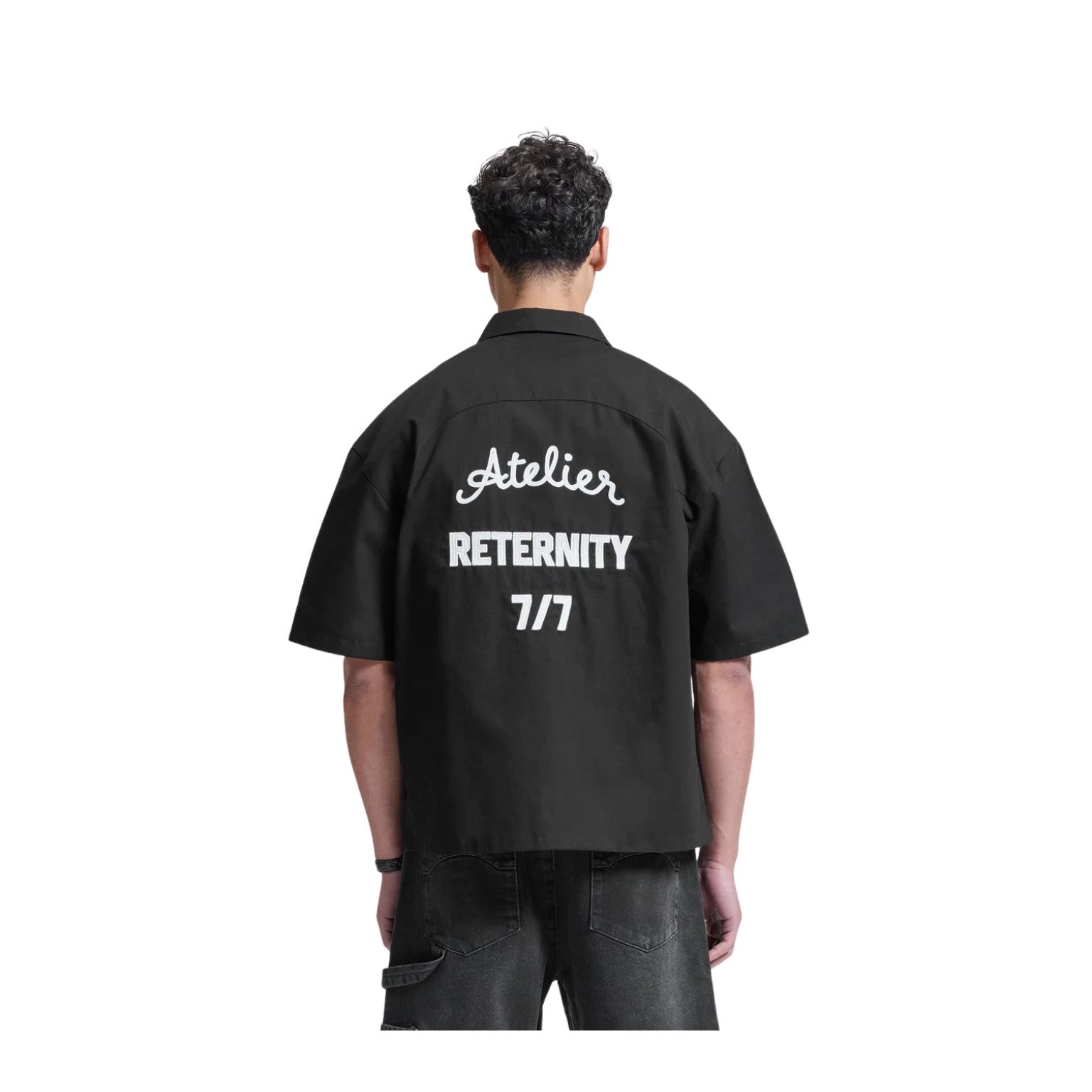 Person wearing a black shirt with white text on the back, standing against a white background